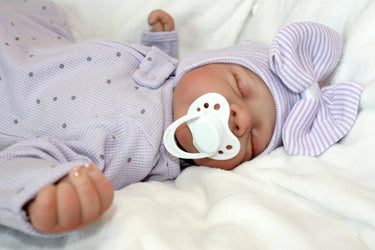 A baby doll with a pacifier lies on a bed, showcasing its soft features and gentle expression.
